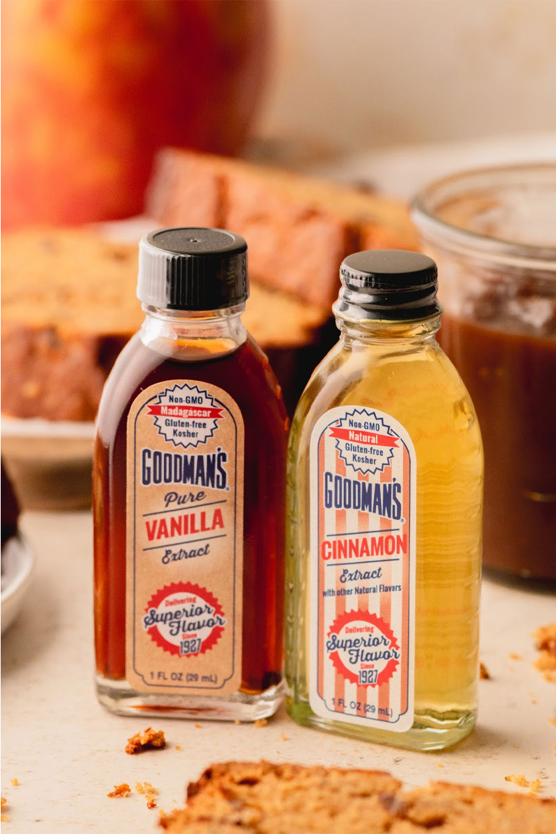 Two bottles of Goodman's vanilla and cinnamon extracts on a table with apple butter bread in the background.