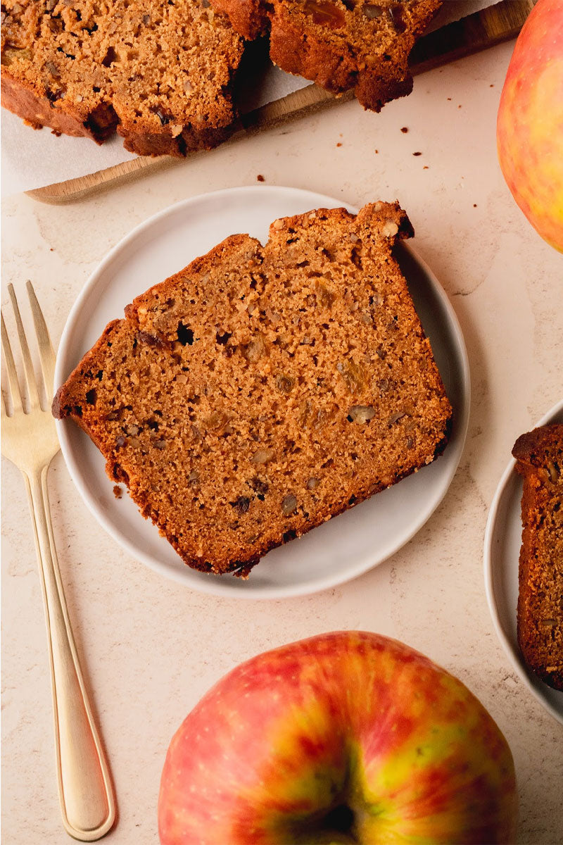 Slice of apple butter bread on a plate with apples and a fork on a light background