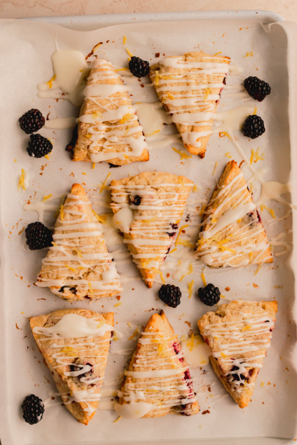 Triangular scones with blackberries and white drizzle on a baking tray