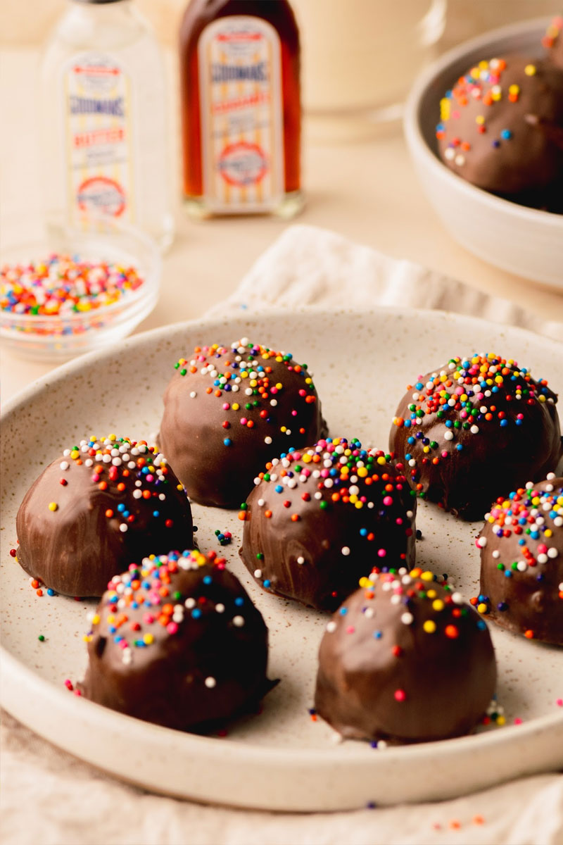 Chocolate bonbons with colorful sprinkles on a plate, with Goodman's extracts in the background