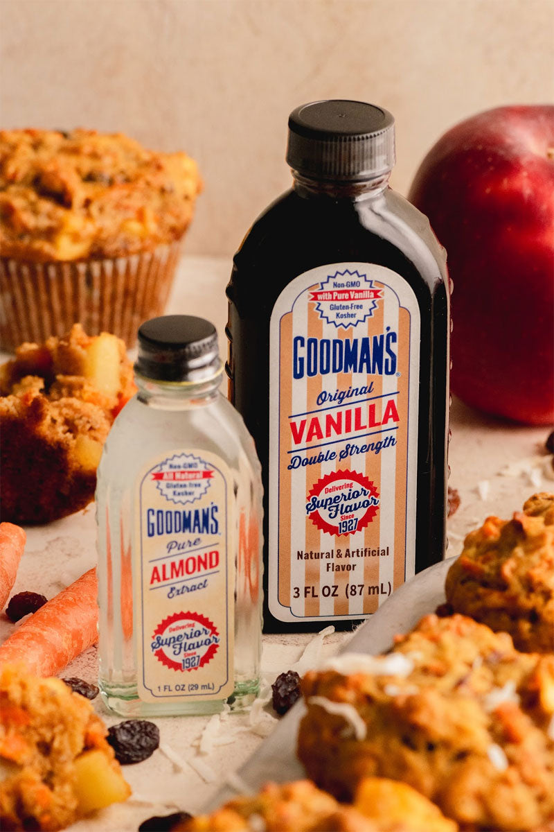 Goodman's vanilla and almond extract bottles with muffins and apples on a wooden surface