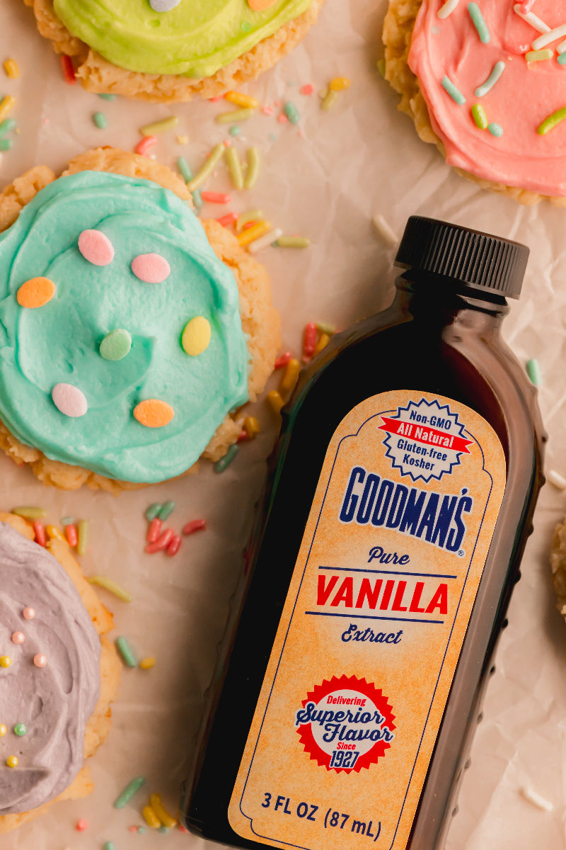 Bottle of Godman's Pure Vanilla Extract with colorful frosted cookies in the background
