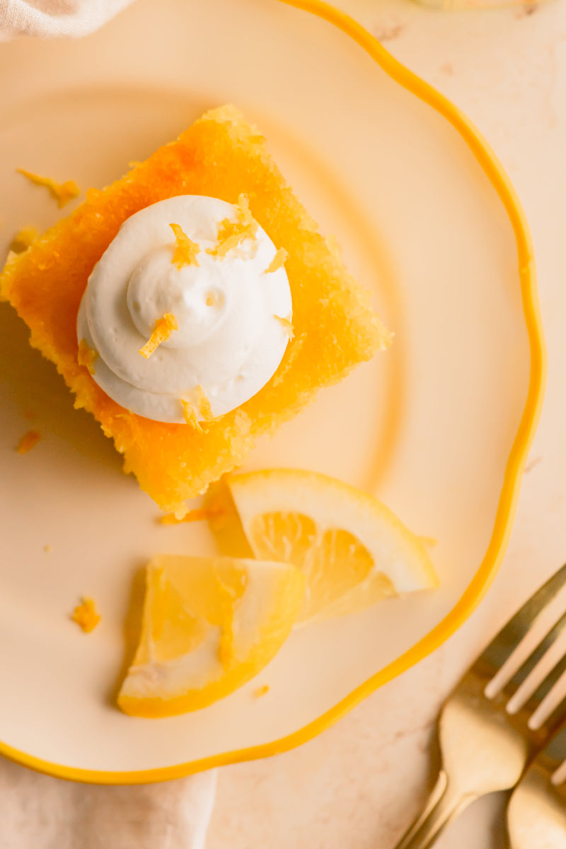 Slice of orange dessert with whipped cream on a decorative plate with lemon slices and a gold fork.