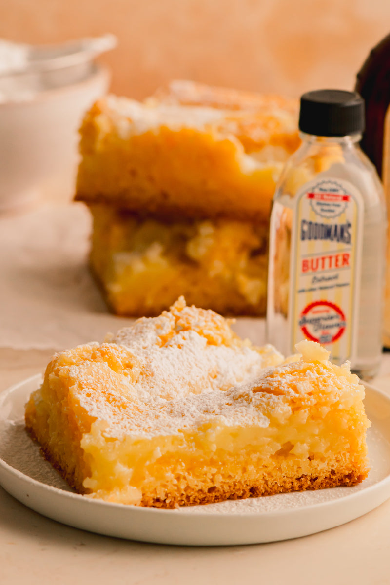 Slice of lemon bar dessert on a plate with a bottle of Goodmans butter in the background.