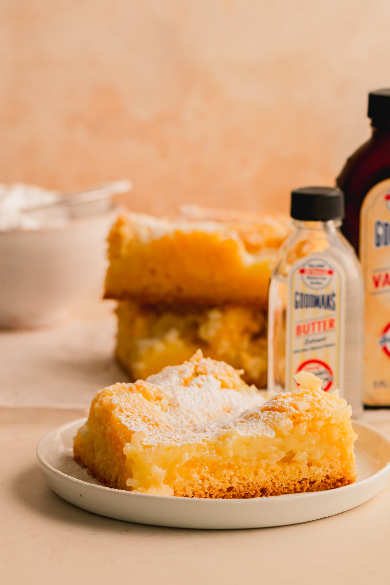 Square of lemon cake on a plate with a bottle of Gorton's Vanilla Extract in the background.