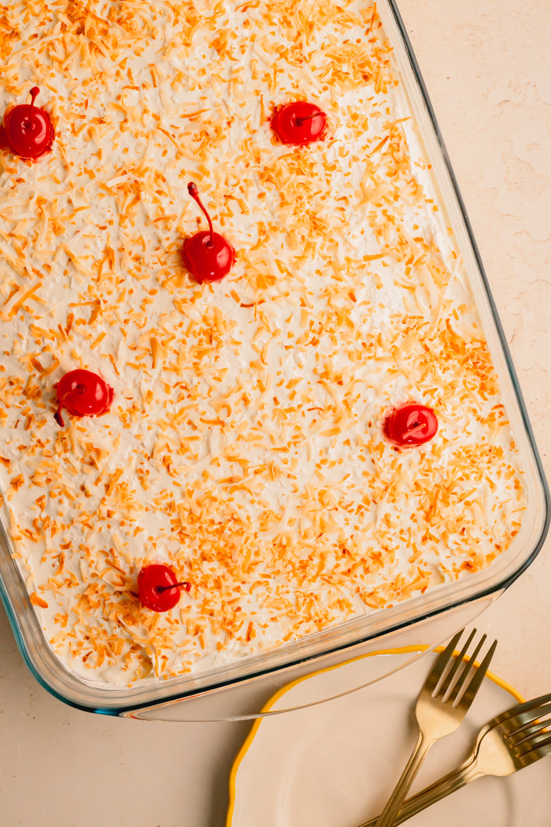 Dessert in a glass dish with shredded coconut and cherries on a beige background
