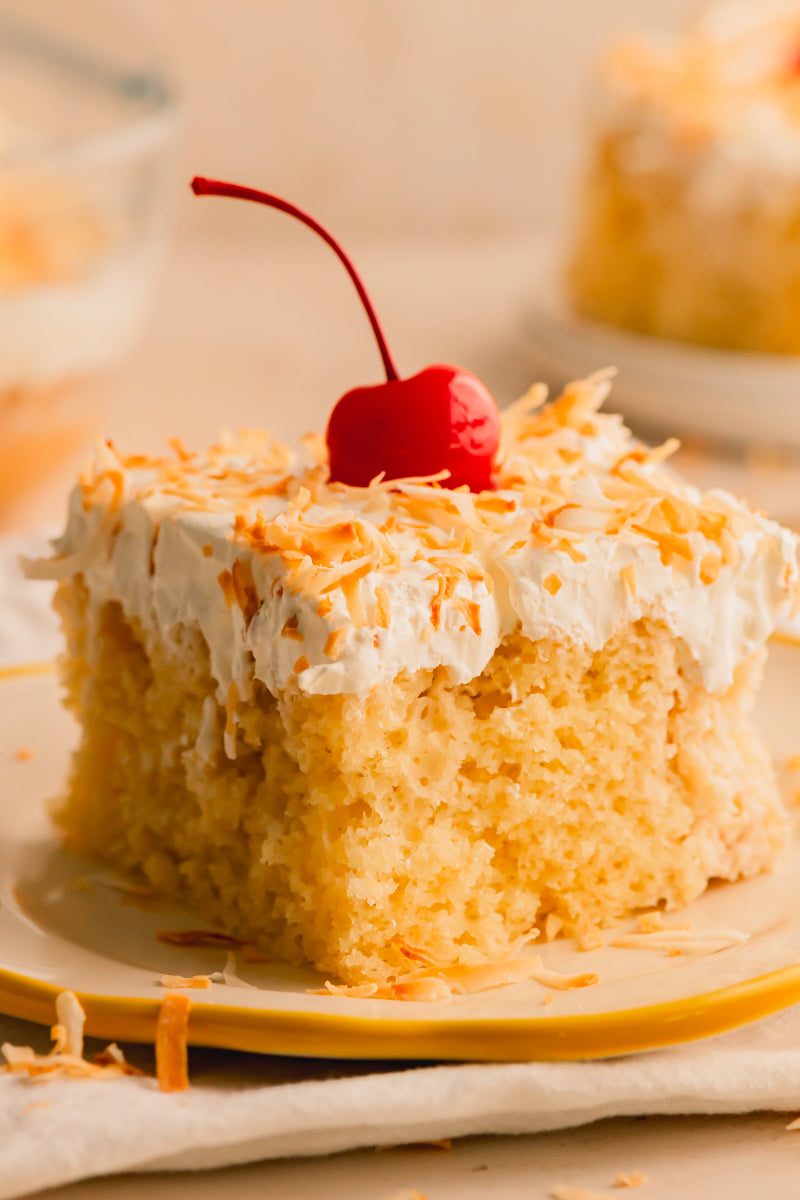 Slice of cake with white frosting and a cherry on top, placed on a plate.