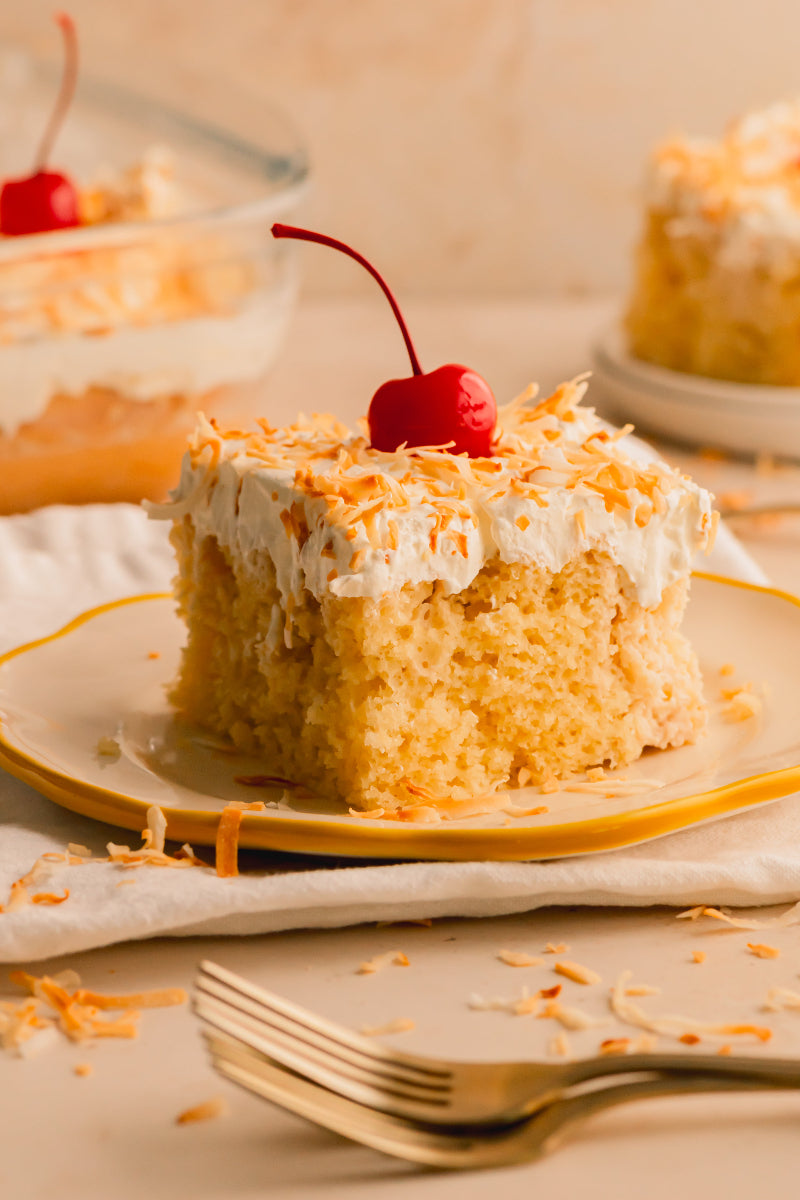 Slice of cake with coconut and a cherry on top, served on a plate.