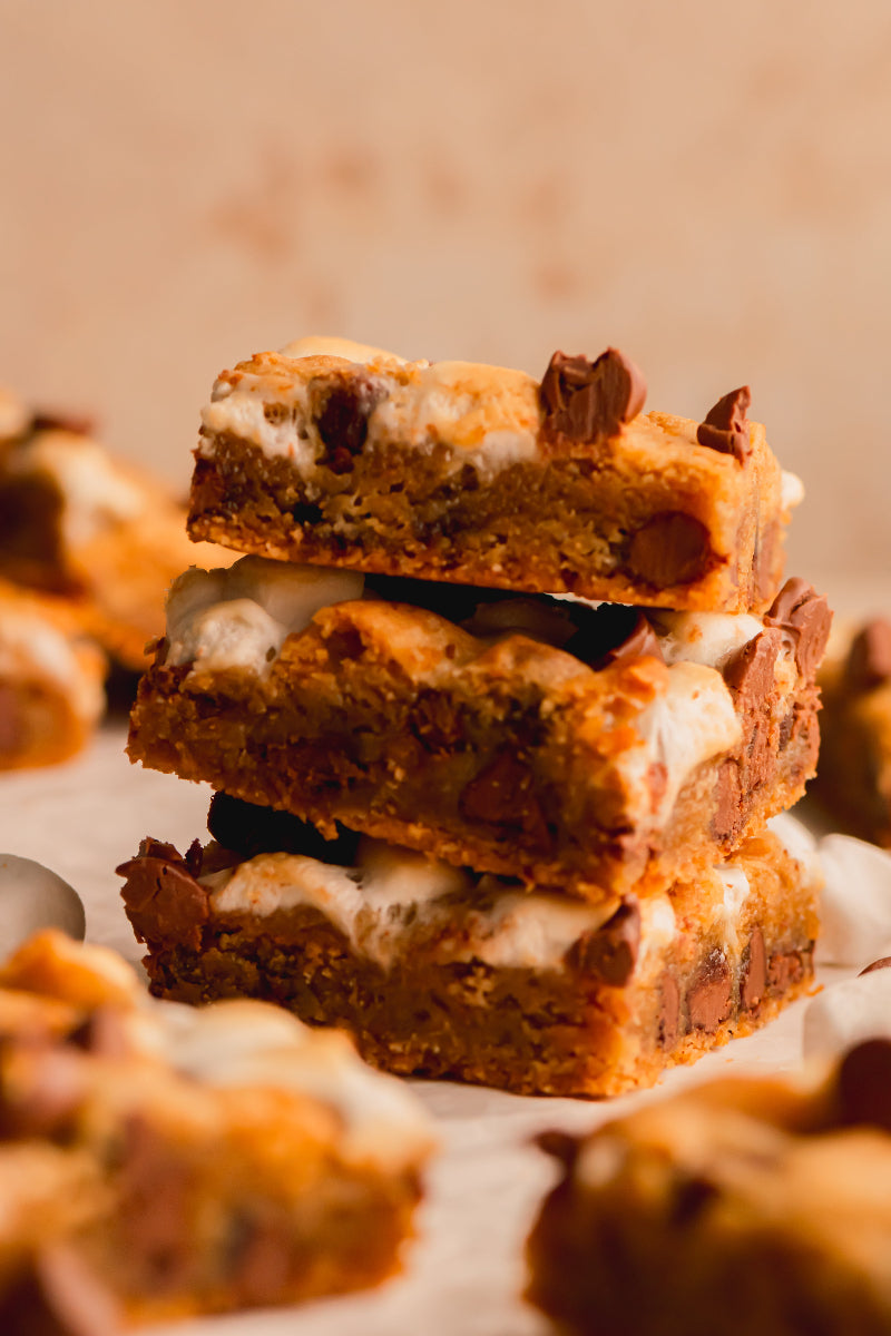 Stack of chocolate chip cookie bars with marshmallows on a white surface.
