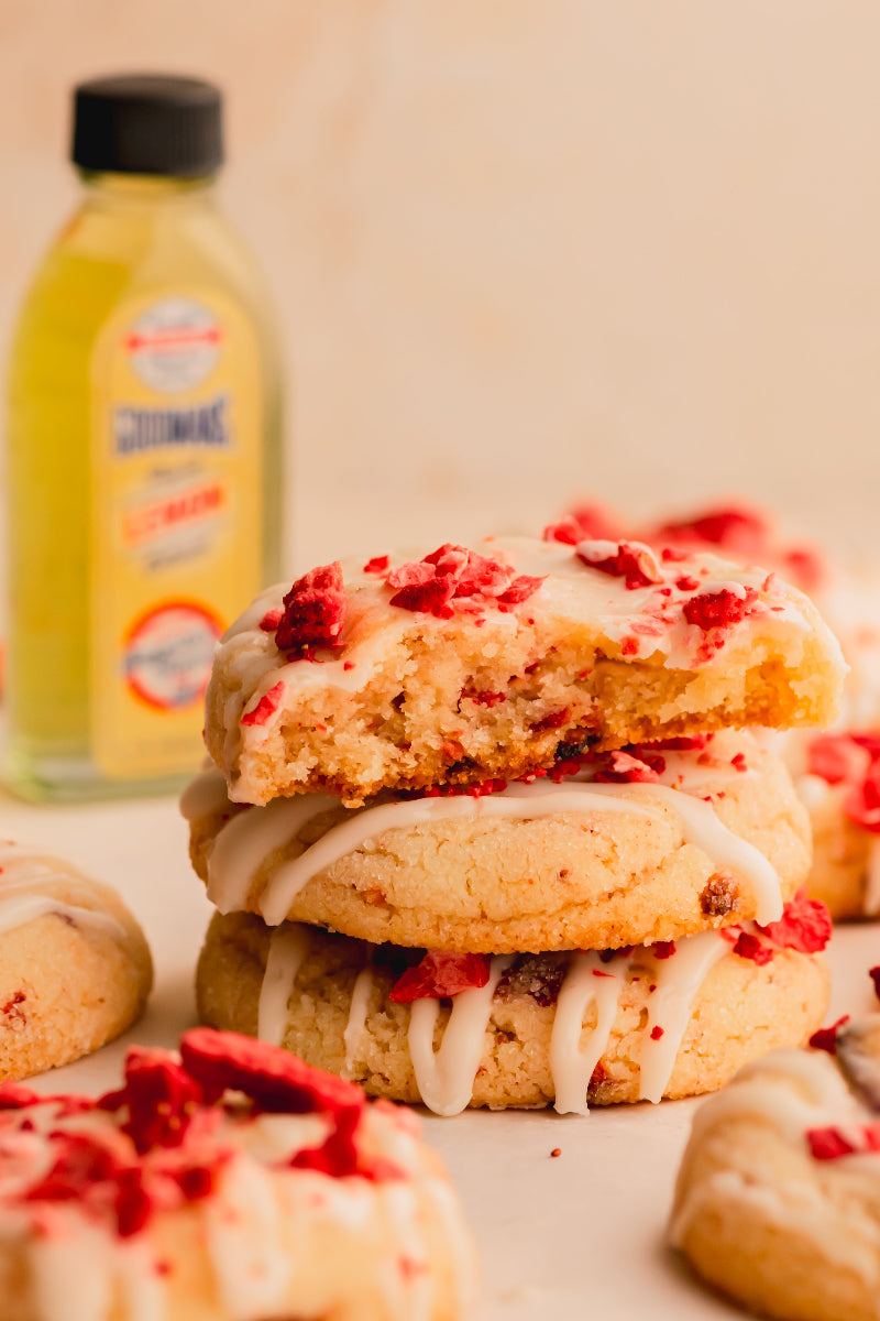 Stack of cookies with white icing and red toppings on a light background with a bottle in the background.