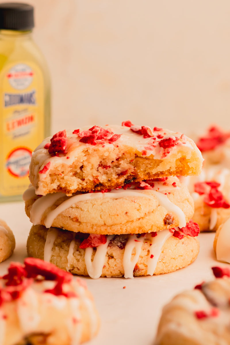 Stack of cookies with white icing and red toppings on a light background