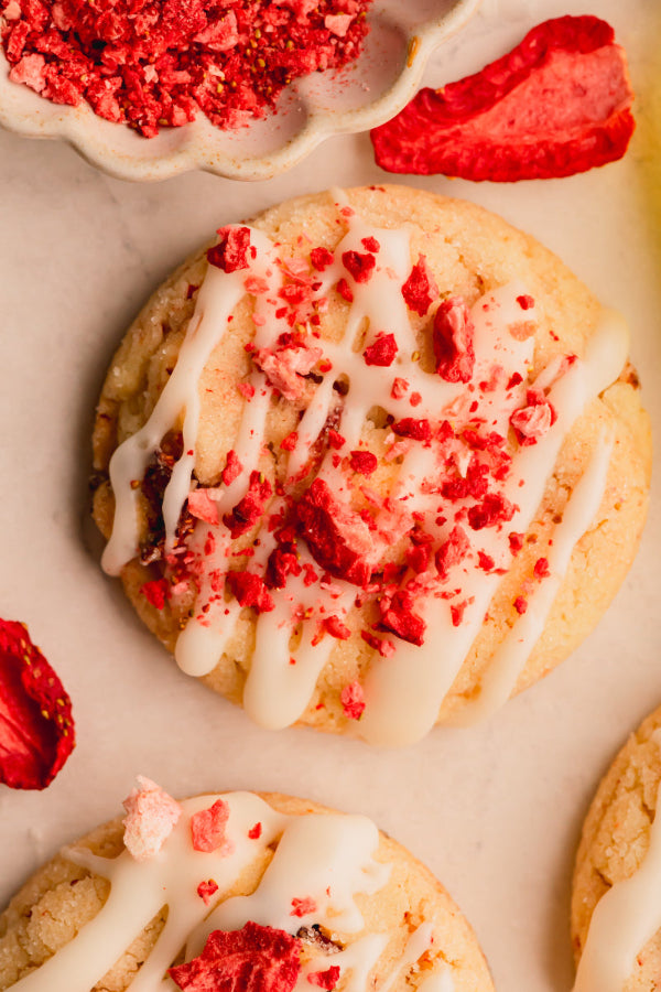 Cookies with white icing and red strawberry pieces on a light background