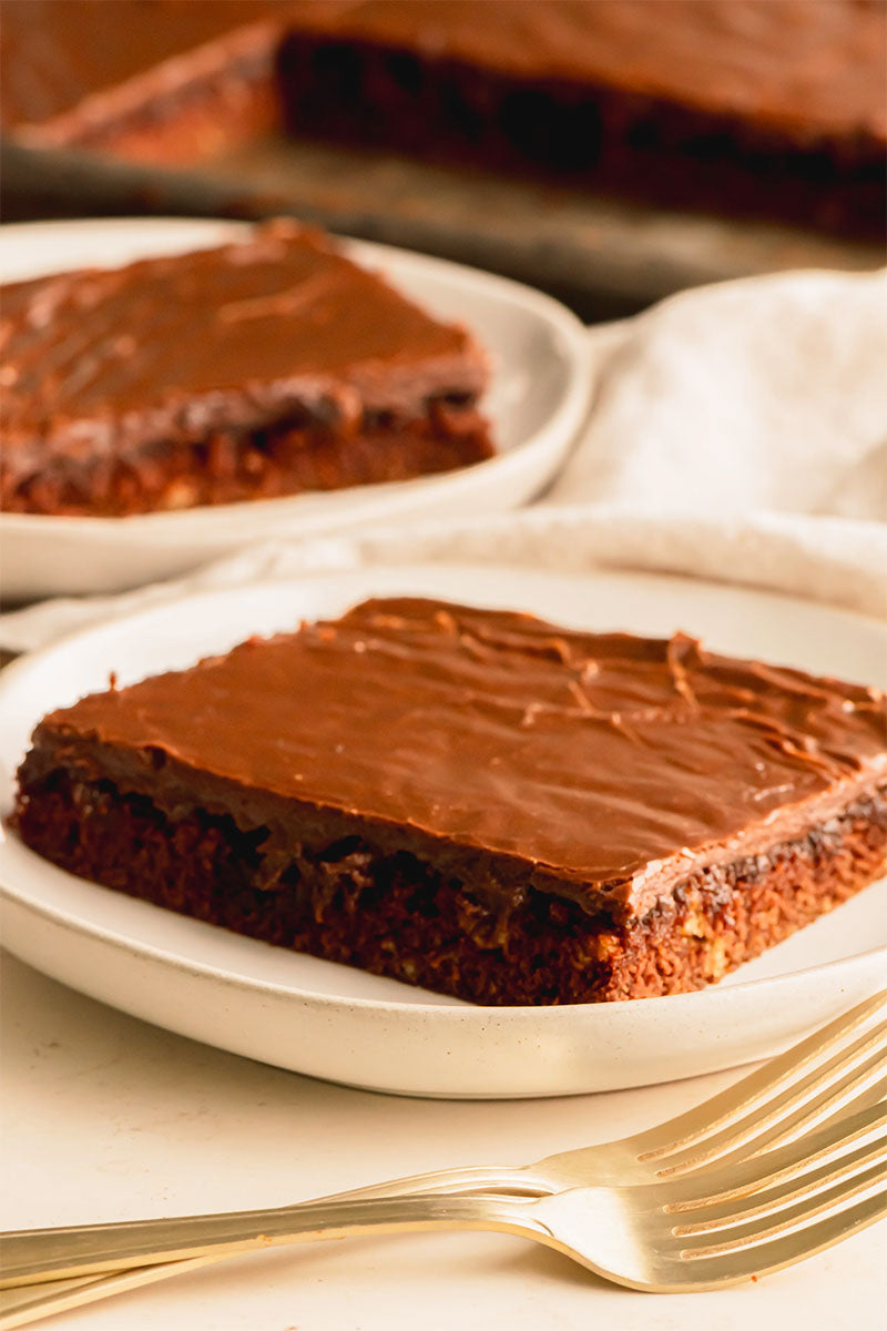 Chocolate frosted brownies on white plates with a fork on a light surface.